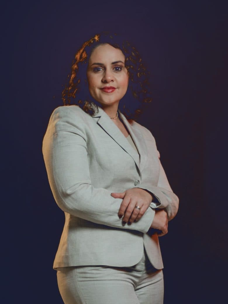 Camila Mota Figueiredo de terno claro e braços cruzados, olhando para a câmera